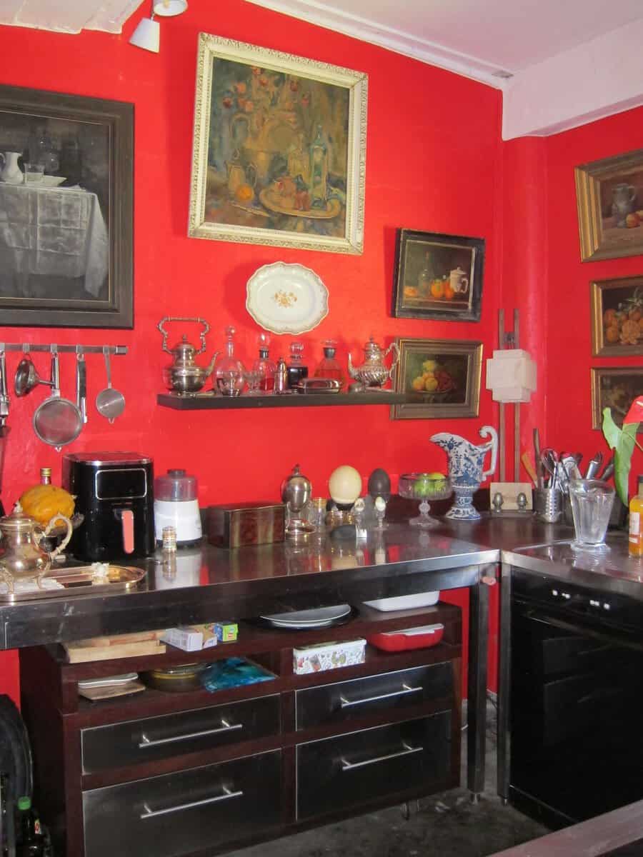 Cuisine aux murs rouges, plans en inox et natures mortes anciennes à l’Habitation de l’Enclos